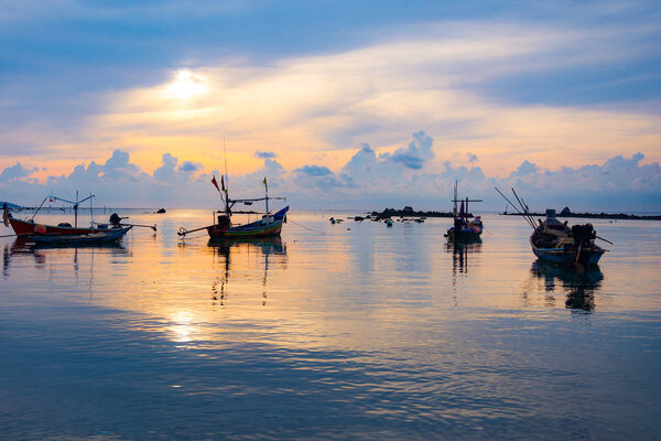 Fishing boat in the sea, sunset and silhouettes of wooden boats 