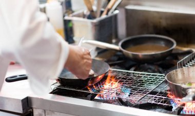 Aşçı, mutfak sobasında tavada alevle yemek pişiriyor.