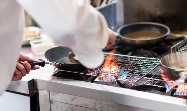 Šéfkuchař vaří s plamenem na pánvi na kuchyňském zápraží — Stock fotografie