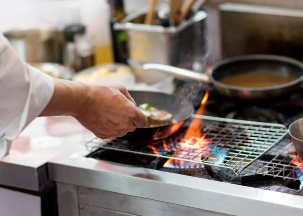 Chef cozinha com chama em uma panela de ato de fritar em um stov de cozinha — Fotografia de Stock