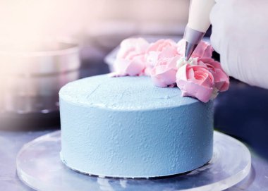 Pasta şefi pastayı süslüyor, şefte pasta poşeti ile krema sıkıyor.