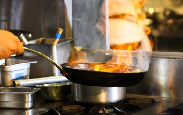 Chef cooking with flame in a frying pan on a kitchen stov