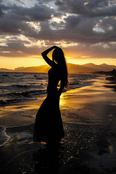 Silhouette of a young, beautiful woman against the background of deserted sea beach. Young women with raised hand on the beach  enjoy the sunset.