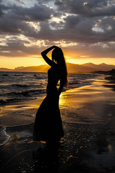  Silhouette of a young, beautiful woman against the background of deserted sea beach. Young women with raised hand on the beach  enjoy the sunset.