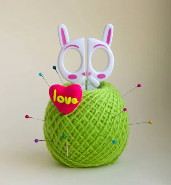 a tangle of green woolen threads, white children\'s scissors in the form of a hare, new port needles with beads, candy in the shape of a heart on a white background. photo