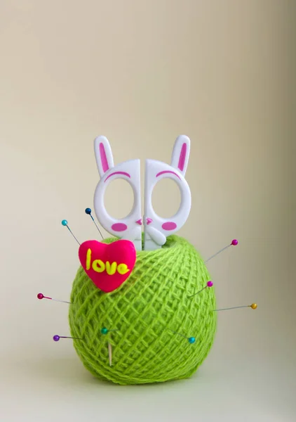 a tangle of green woolen threads, white children\'s scissors in the form of a hare, new port needles with beads, candy in the shape of a heart on a white background. photo