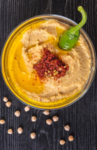 Hummus with hot pepper on a black wooden background