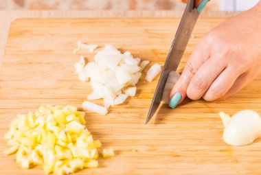 Cook cuts onions with a knife on wooden board clipart