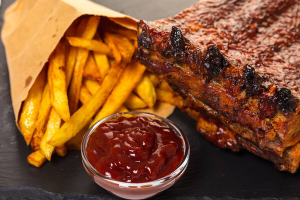 grilled ribs with fries and sauce on a black background