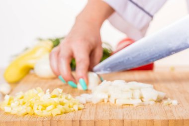 Cook cuts onions with a knife on wooden board clipart