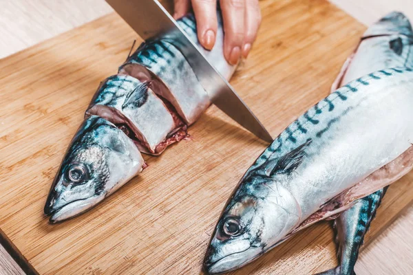 cook cuts raw mackerel fish, hands closeup