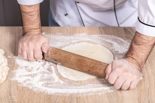 male cook kneads dough on the table