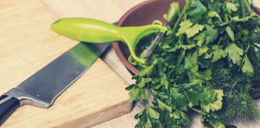 Maydanoz ve dereotu kesme tahtasının üzerinde bir bıçakla yatıyor.