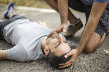 Adam bir kişiye asfalt üzerinde ilk yardım verir