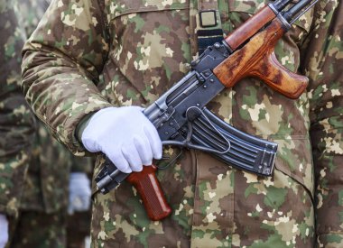 Asker eliyle silah üzerinde beyaz bir eldiven giymiş.