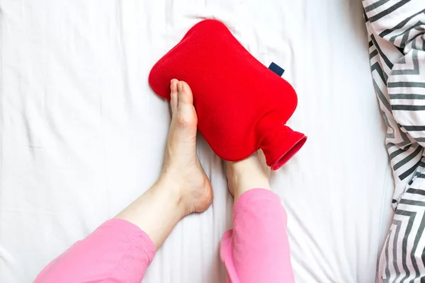 Woman with cold feet in bed on a red hot water bottle