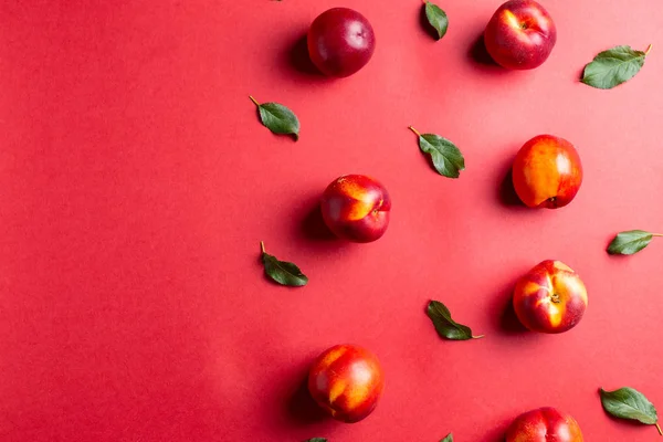 Nectarinas e folhas na mesa de fundo vermelho — Fotografia de Stock