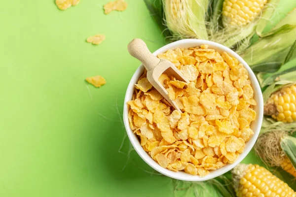 Kukuřičné vločky a kukuřičné kobky přes zelené pozadí, zdravé jídlo co — Stock fotografie
