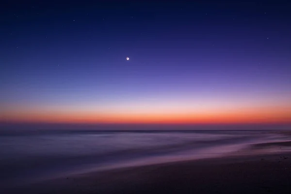 Larga exposición en la playa una noche con el mes antes del sol —  Fotos de Stock