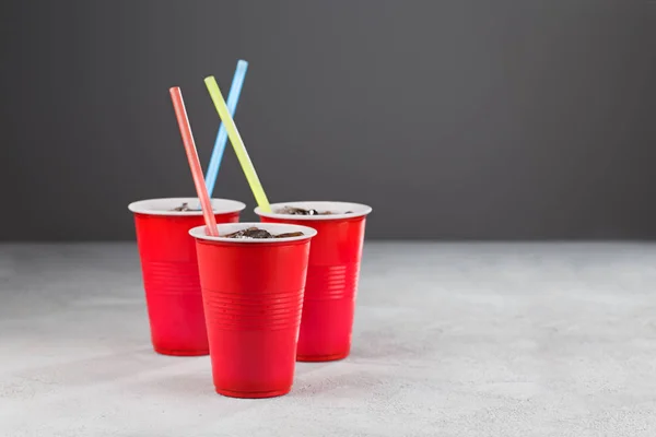 Three red cups with soda and colored straws on a gray background. Closeup.