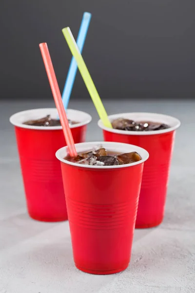Three red cups with soda and colored straws on a gray background. Closeup.