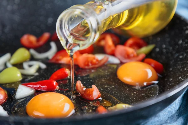 close-up shot of eggs on frying pan with tomatoes and onion while oil pouring from above