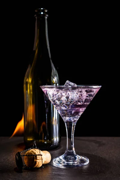 close-up shot of glass of pink alcoholic drink with bottle on black surface with fire