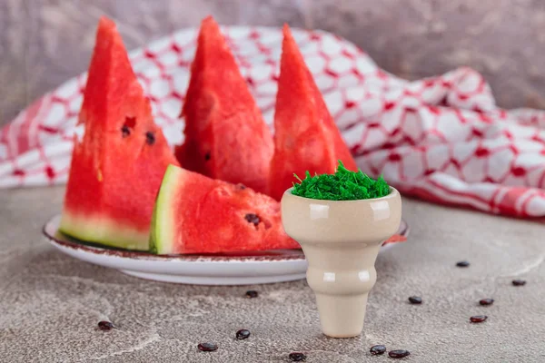 mix for Smoking a hookah with mint flavor in a hookah bowl on the background of ripe pieces of watermelon