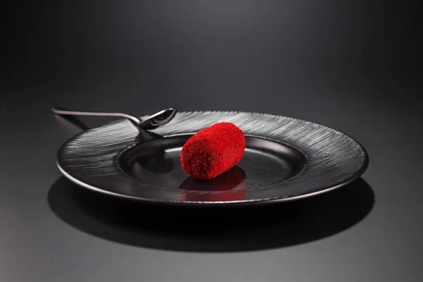 miniature cake-potatoes with red sprinkles on a black plate. Selective focus.