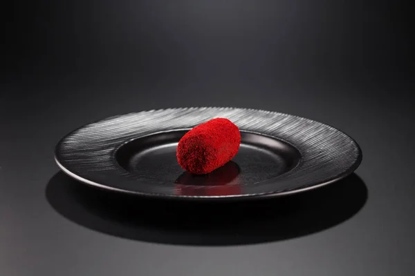 miniature cake-potatoes with red sprinkles on a black plate. Selective focus.