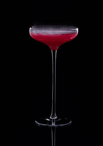 Cocktail based on carbonated drink in a beautiful glass on a thin long leg isolated on black with reflection. Selective focus.