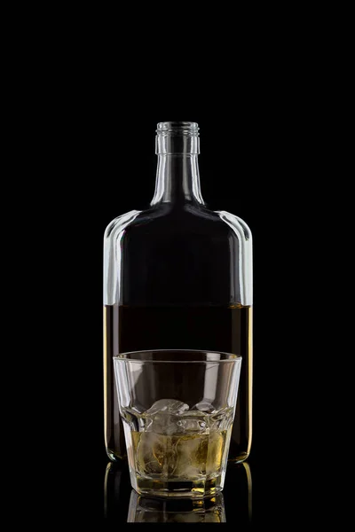 Bottle of whiskey and a glass of whiskey with ice cubes standing in front of her, isolated on a black background with reflections. 100 sharpness. Vertical.