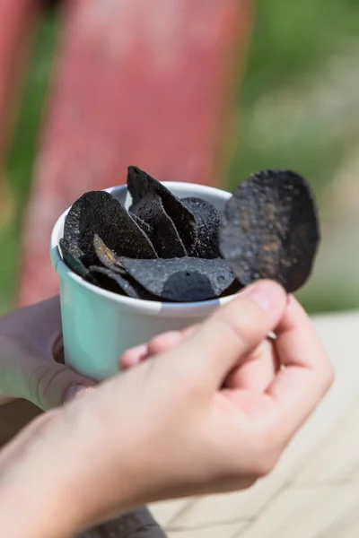 Black chips. Black potato chips in the hands of a teenager on the background of a sunny summer landscape.