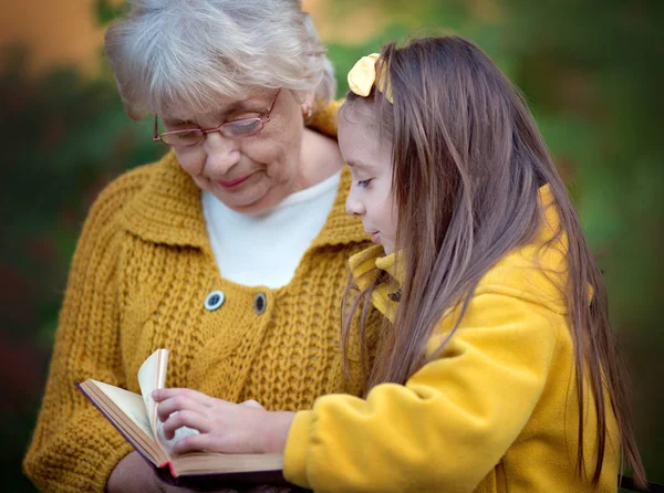 祖母与孙女读书在秋天公园 — 图库照片