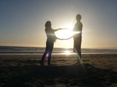 gökyüzünde güneşin üzerinde el ele tutuşan siluetli çift