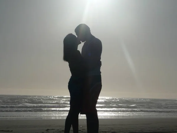 silhouette of couple standing and kissing by sea