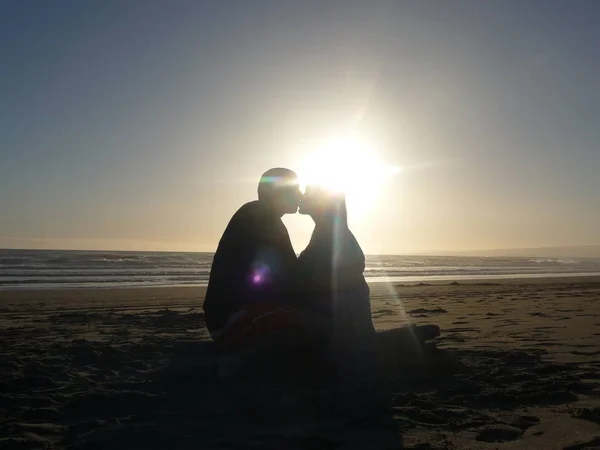 silhouette of couple sitting and kissing on sand by sea