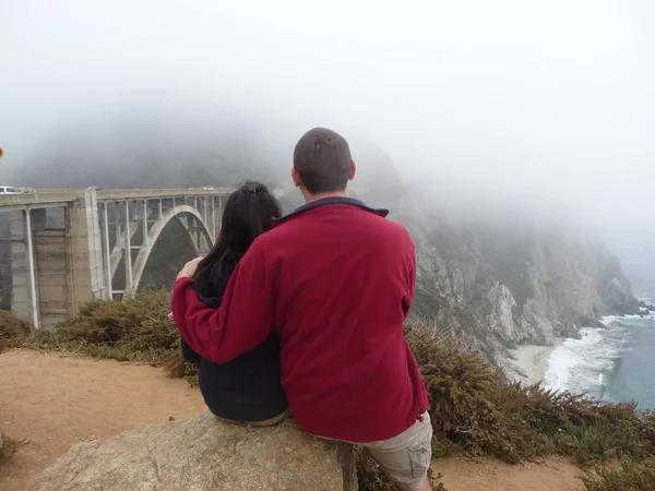 Pareja Sentada Colina Por Puente Las Rocas Sobre Mar Cubierto — Foto de Stock