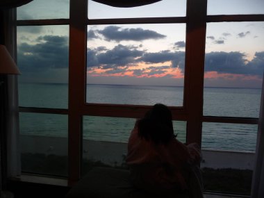 gün batımı manzaralı pencerede oturan kadın