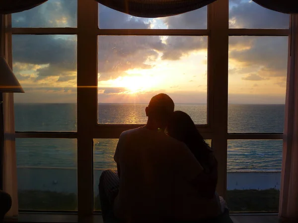 couple hugging by window with sunset view