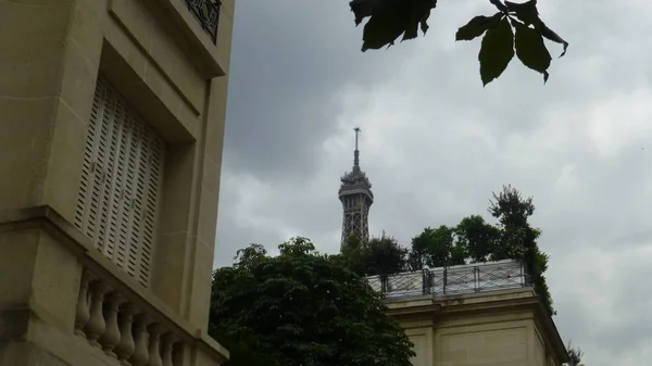 top of eiffel tower seen through greenery and houses