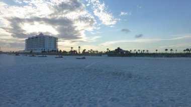 bulutlu gün batımı gökyüzü altında binalar ve avuç içi ile kumlu plaj görünümü