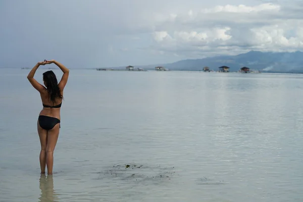 比基尼泳装的妇女的后视镜摆姿势与提高的手在海滩上 — 图库照片