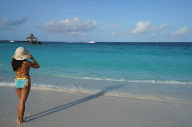 gün batımında sahilde duran şapka ve bikini giyen kadın