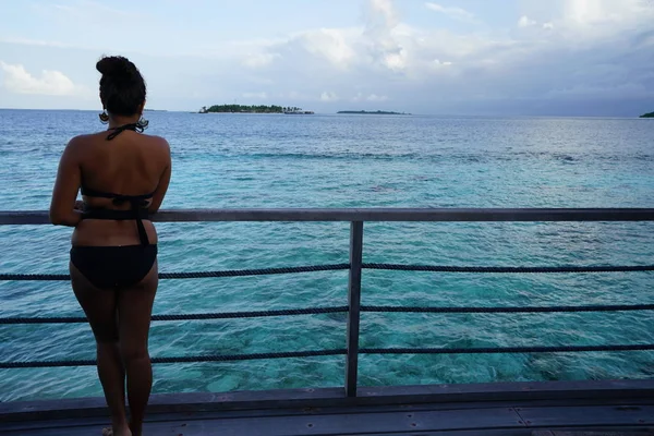 rear view of woman wearing bikini standing by fence with marine view