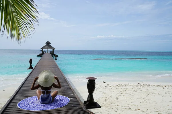 熱帯シーンで木製の桟橋の上に座って帽子をかぶっている女性 — ストック写真