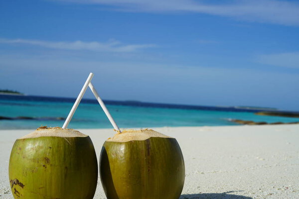 two coconuts with straws on sandy beach surface