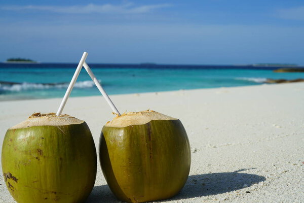 two coconuts with straws on sandy beach surface