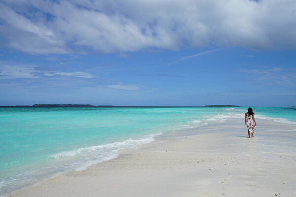 rear view of woman wearing dress walking at blue bay