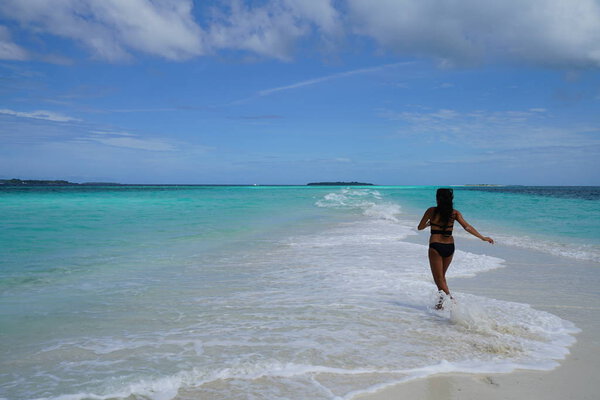 rear view of woman wearing bikini running at blue bay